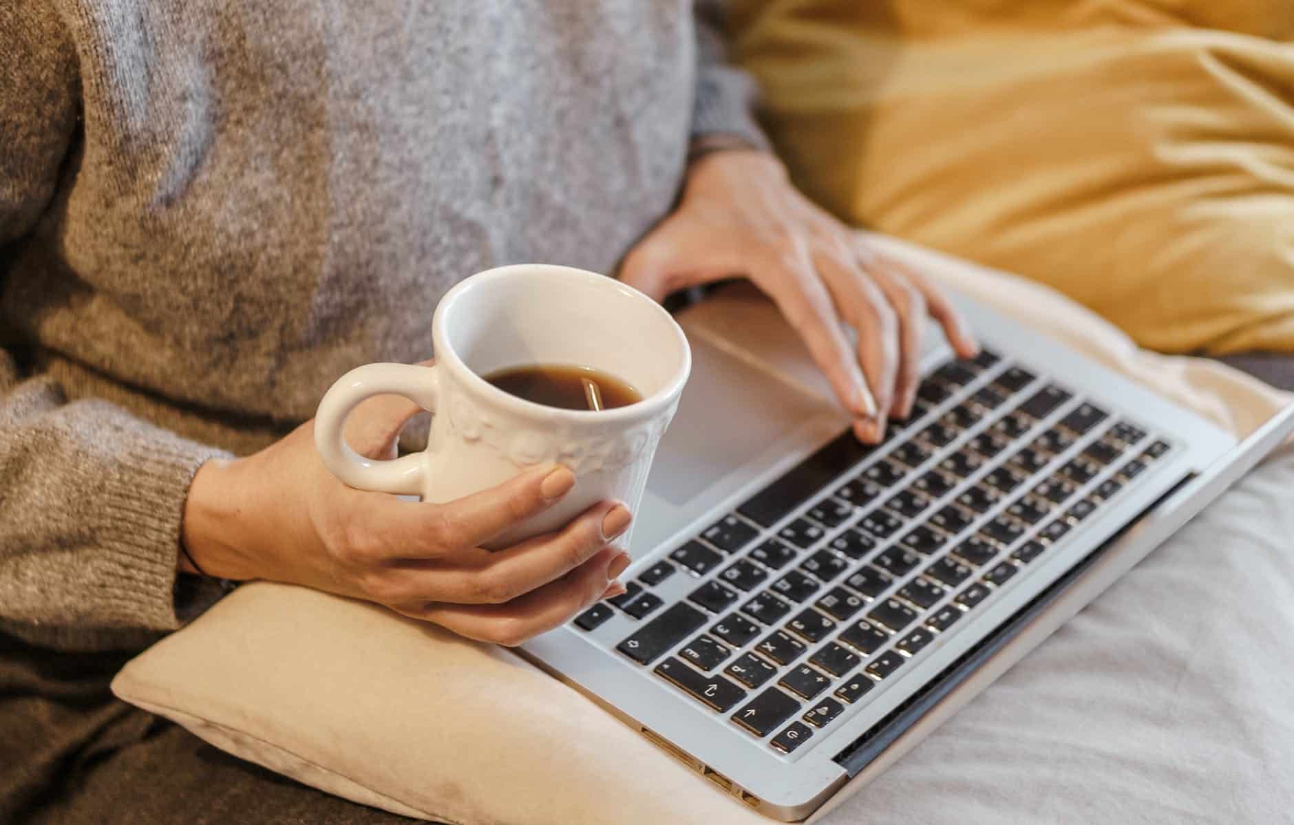 crop freelancer with mug of coffee typing on laptop